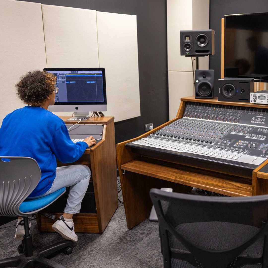 student sitting at a Mac in music studio with PA equipment