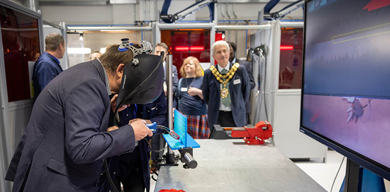 Stem Centre launch demonstration at RuTC - one of the councillors is wearing a black helmet and testing some of the equipment with a large screen in front of him and poeple looking on.  