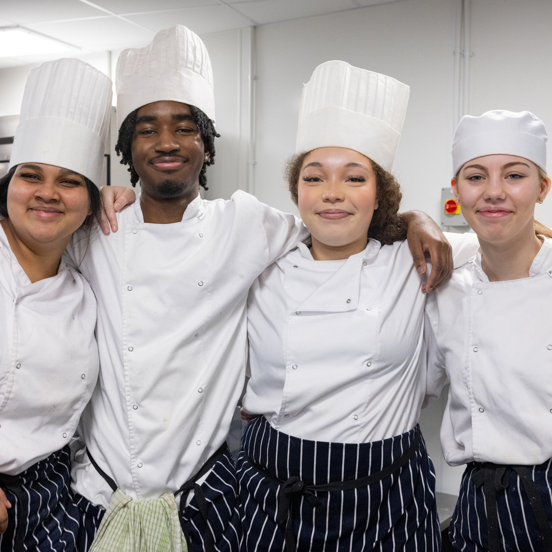4 professional cookery students with their arms around each other smiling at the camera